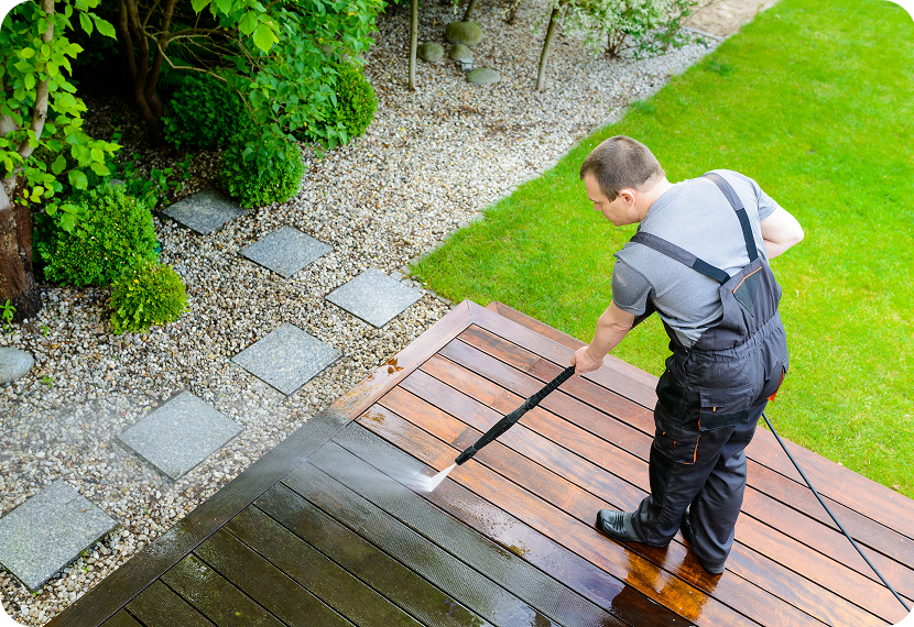 Man pressure washing wooden deck outside.